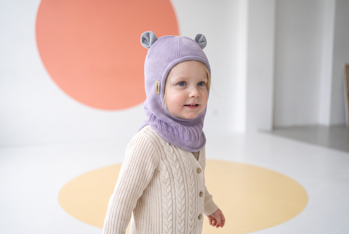 Barn iført Lavendel elefanthue i merinould fra Lumily med strikkede bjørneører, i lyst studiemiljø